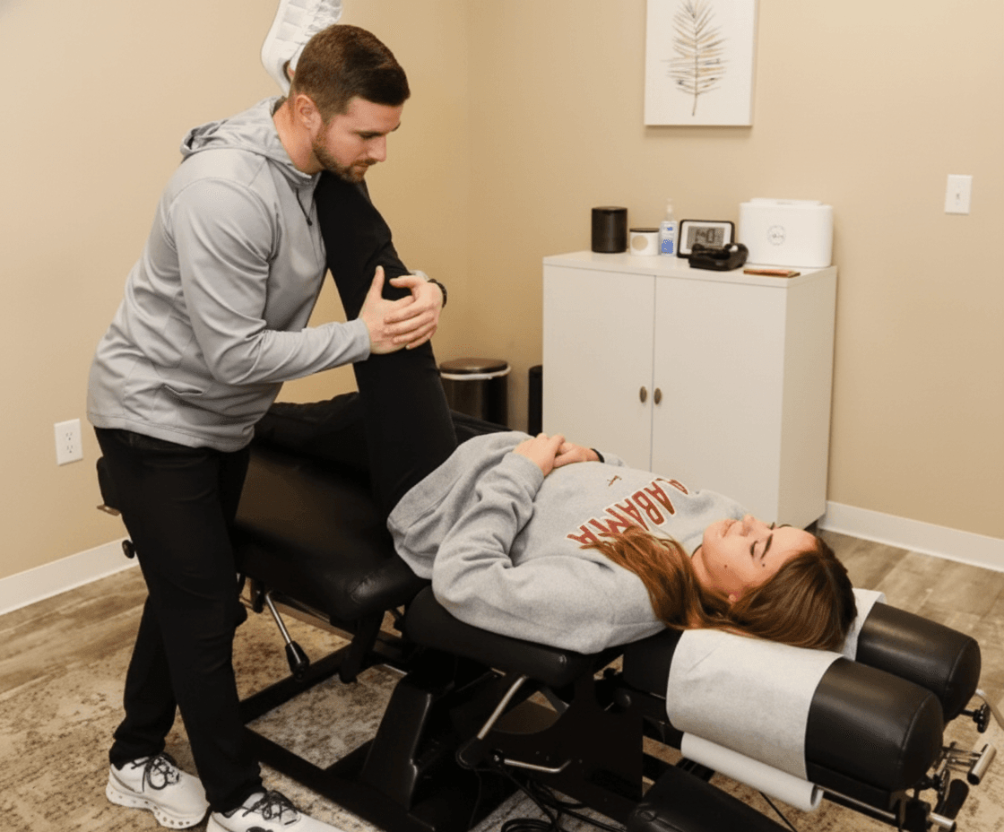 A male chiropractor stretches the leg of a female patient lying face up on a treatment table in a modern clinic room.