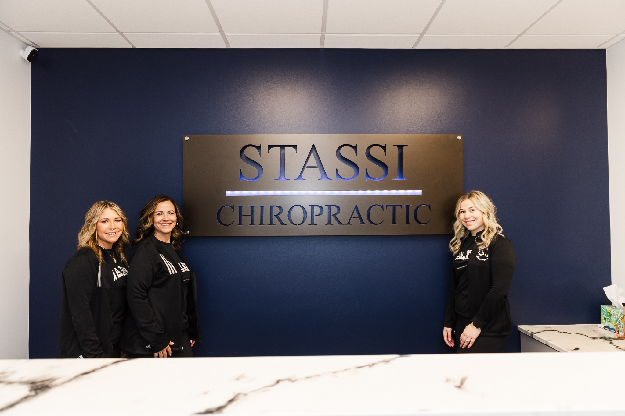 Four smiling Stassi Chiropractic team members, three women and one man, in branded black apparel.
